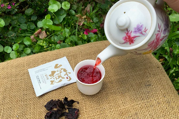 茶壺倒入紅色茶湯，旁有乾燥原料與包裝